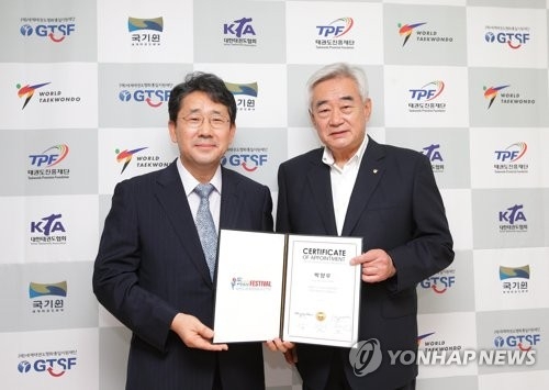 In this photo provided by the World Taekwondo on July 27, 2017, the WT President Choue Chung-won (R) holds a certificate with Park Yang-woo, the chief organizer of the Taekwondo Peace Festival, at his office in Seoul. (Yonhap)
