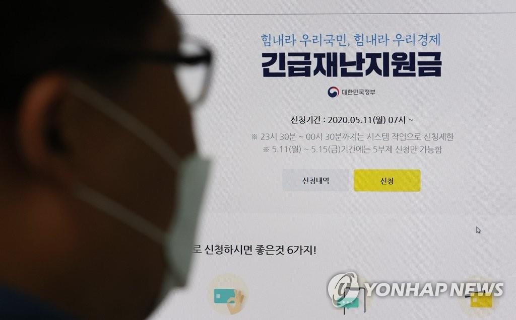 The undated photo shows a masked bypasser looking at an information poster about the government's emergency relief fund. (Yonhap)