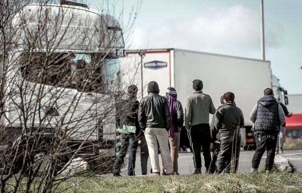 프랑스 칼레 항구를 지나는 트럭 사이로 보이는 이민자들.