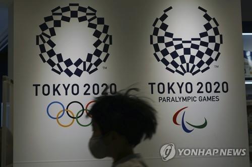 (도쿄 AP=연합뉴스) 23일 일본 도쿄도에 설치된 도쿄 올림픽·패럴림픽 홍보물 앞으로 마스크를 쓴 사람이 지나가고 있다.