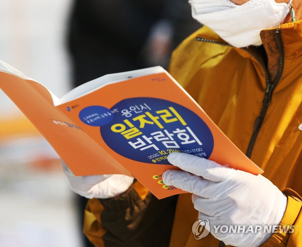 Wearing a mask and plastic gloves, a jobseeker reads a pamphlet at a job fair in Yongin, just south of Seoul, on Oct. 21, 2020.