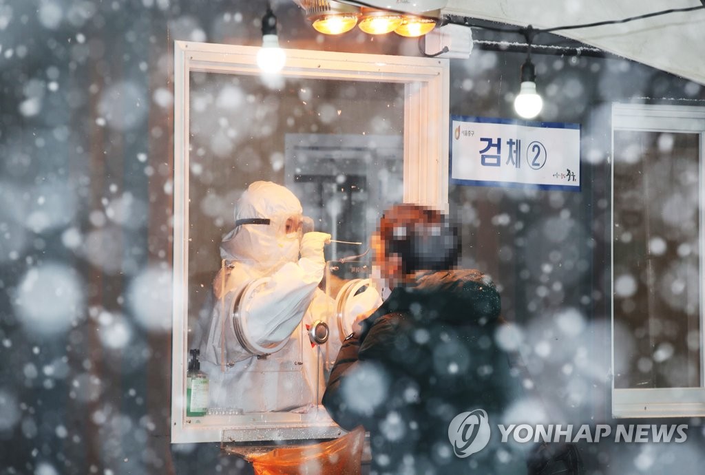 雪が降りしきる中、ソウル駅前の広場の臨時検査所で新型コロナウイルスの検査を受ける市民＝１２日、ソウル（聯合ニュース）