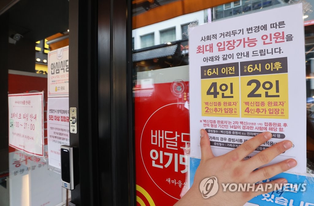 This photo taken on Oct. 17, 2021, shows a worker attaching a notice on the revised social distancing rules on the window of a restaurant in Seoul. (Yonhap)