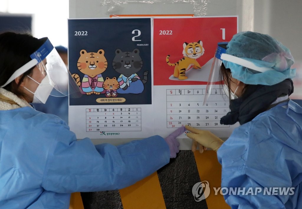 Medical workers talk to each other while pointing to calendars for 2022, the Year of the Tiger in the Chinese zodiac, as they prepare to administer coronavirus tests at a screening clinic in the southwestern city of Gwangju on Dec. 30, 2021. (Yonhap)