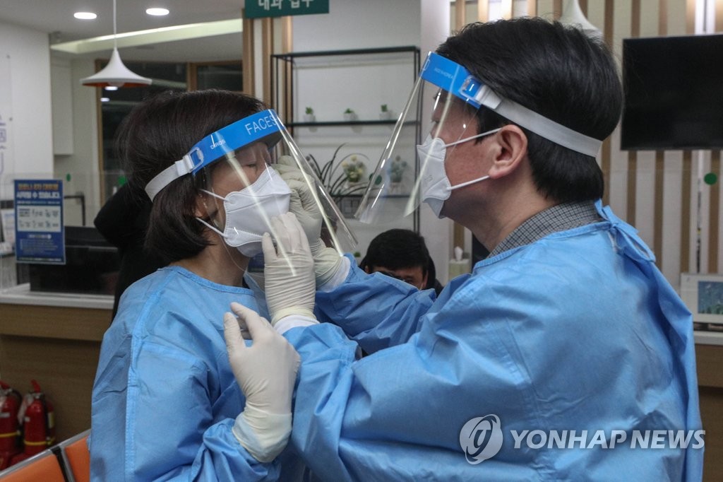 Ahn Cheol-soo (R), the presidential candidate of the minor opposition People's Party, helps his wife Kim Mi-kyung put on a protective mask before they start volunteer work at a coronavirus testing center in Seoul, on Feb. 19, 2022. (Pool photo) (Yonhap)