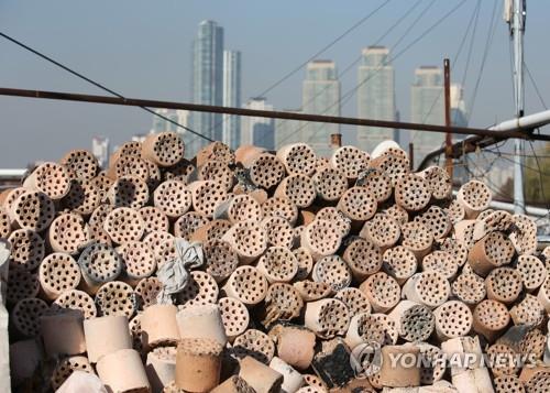 This photo, taken Dec. 8, 2015, shows piles of used charcoal briquettes, mainly used for heating by people in poor neighborhoods, against the backdrop of high-rise residential buildings in Gangnam, the most expensive district in Seoul. (Yonhap)