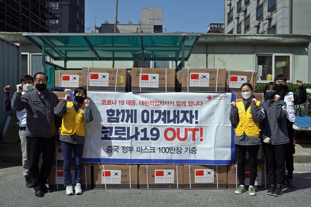 In this photo provided by the Red Cross on March 31, 2020, staff members of the Red Cross pose in front of surgical masks Beijing delivered to Seoul last week as part of relief efforts for the fight against the new coronavirus. (PHOTO NOT FOR SALE) (Yonhap)