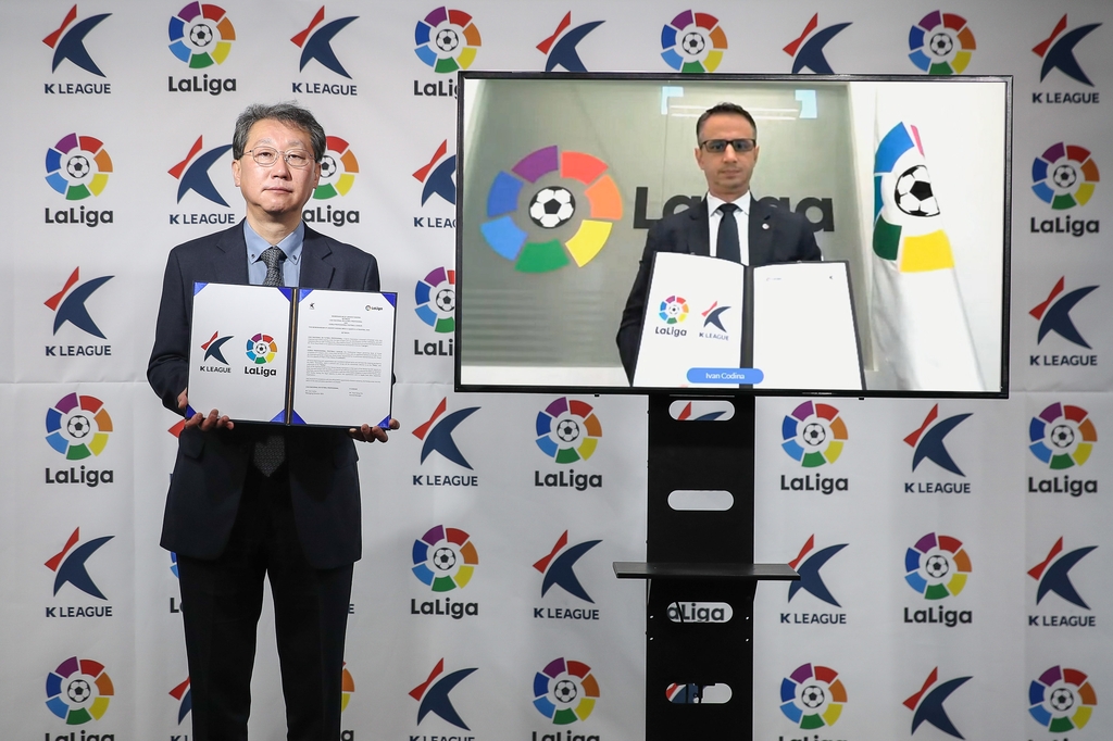 Cho Yeon-sang (L), secretary general of the Korea Professional Football League (K League), holds a partnership agreement signed with La Liga of Spain in a virtual ceremony held in Seoul, while Ivan Codina, managing director of Southeast Asia for La Liga, does the same in his Singapore office on Dec. 10, 2020, in this photo provided by the K League. (PHOTO NOT FOR SALE) (Yonhap)