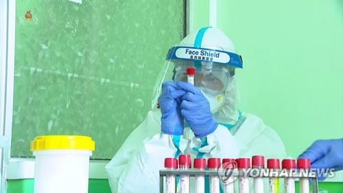 In this photo from the North's Korean Central Television on May 20, 2022, a medical worker wearing protective gears looks at a specimen container of a COVID-19 test swab. (For Use Only in the Republic of Korea. No Redistribution) (Yonhap)
