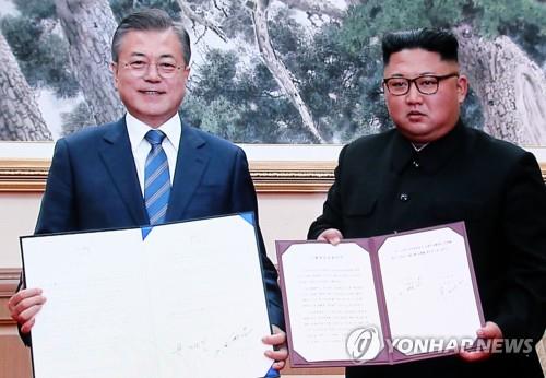 共同宣言に署名した文大統領（左）と金委員長。会談のためソウルに設置されたプレスセンターのモニターから＝１９日、ソウル（聯合ニュース）