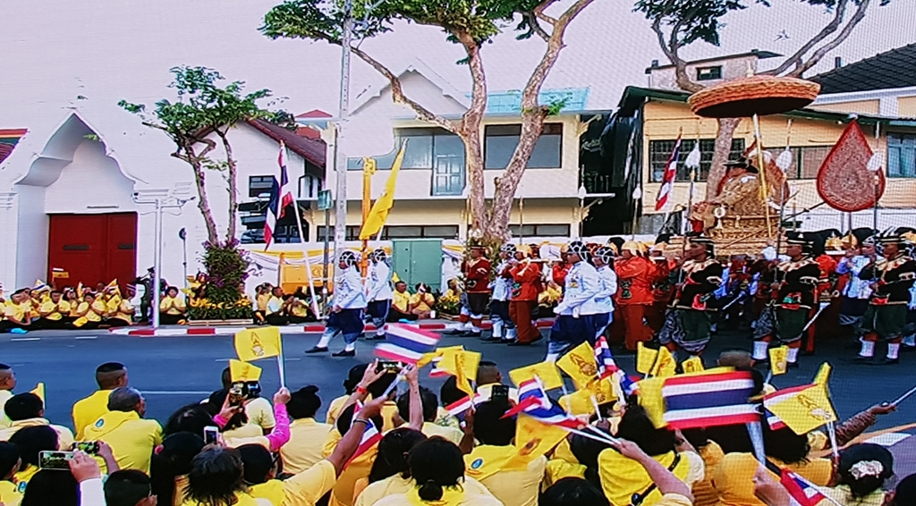 국왕이 탄 가마가 지나가자 태국 국기와 왕실기를 흔들며 환영하는 시민들