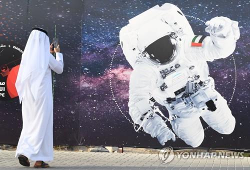 MBRSC에 전시된 UAE 국기를 단 우주비행사 그림 앞에서 사진을 찍는 장면 