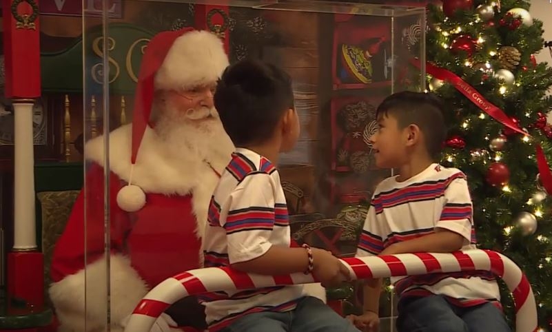 유리벽을 사이에 두고 산타의 무릎에 앉아 얘기를 나누고 있는 두 어린이
