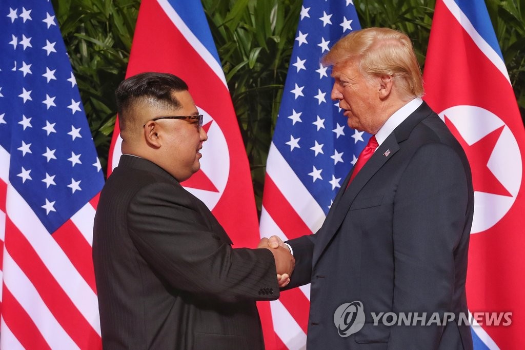 This photo, provided by Singapore's communications and information ministry on June 12, 2018, shows U.S. President Donald Trump (R) making a historic handshake with North Korean leader Kim Jong-un ahead of their first summit in Singapore. (Yonhap)