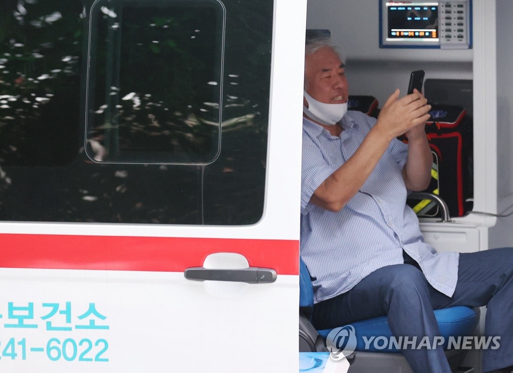 Rev. Jun Kwang-hoon looks at his mobile phone while waiting to be transported to a nearby hospital for new coronavirus treatment on Aug. 17, 2020. (Yonhap)