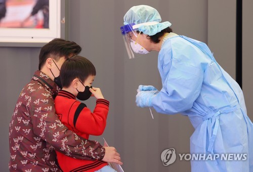 ソウル駅の広場に設置された新型コロナウイルスの臨時検査所で父親の膝に乗せられて検査を受ける子ども＝２５日、ソウル（聯合ニュース）