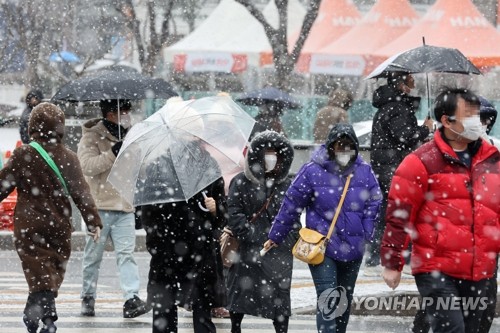 雪が降る中を歩く市民＝１９日、ソウル（聯合ニュース）