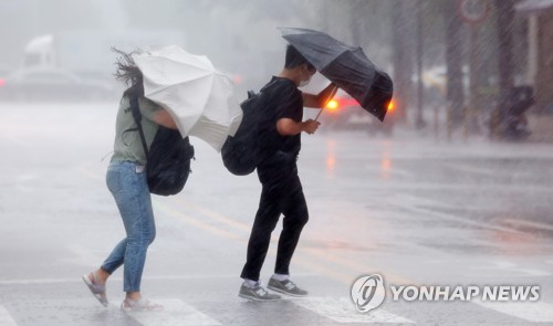 大雨の中、横断歩道を渡る市民＝８日、ソウル（聯合ニュース）