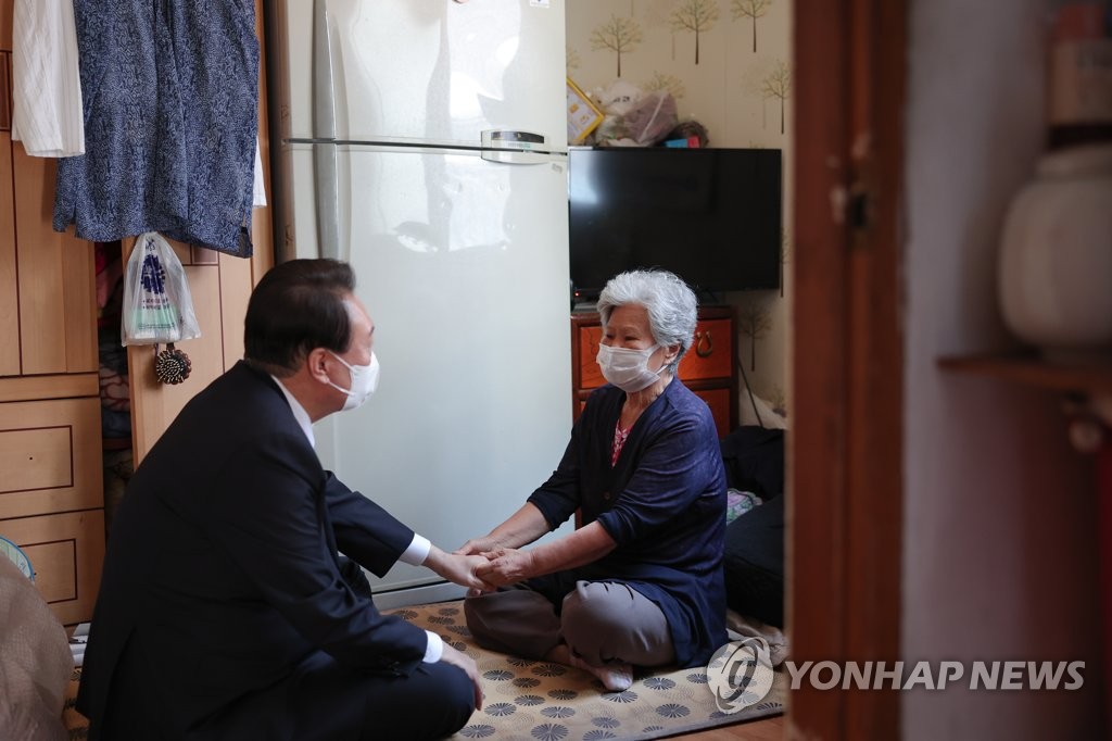 President Yoon Suk-yeol (L) holds hands with a senior citizen who lives alone while depending on government subsidies in Changsin-dong, Seoul, on Sept. 1, 2022. (Yonhap)