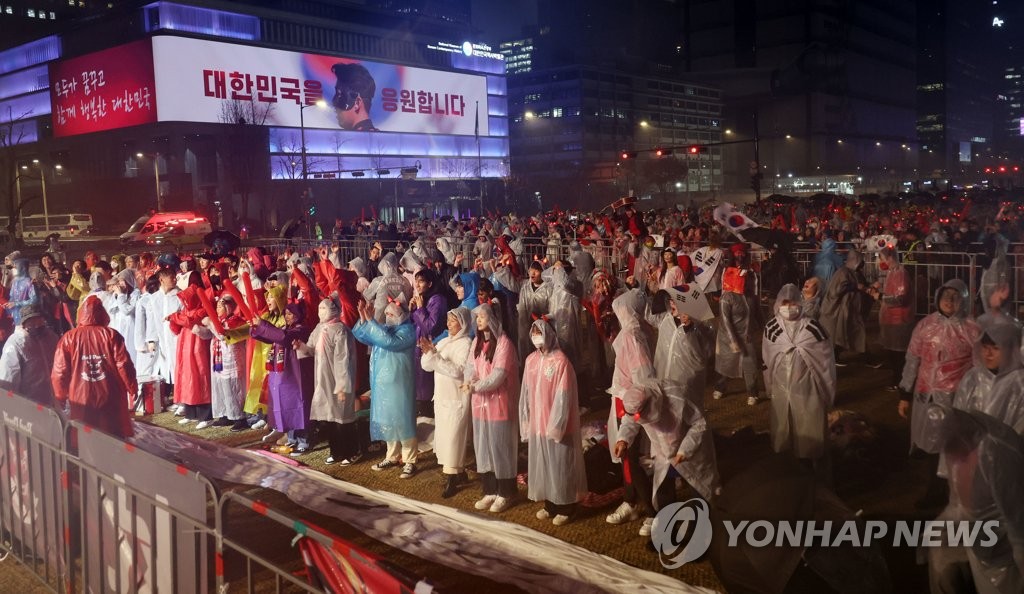 １１月２８日夜、雨が降る中、ソウル中心部の光化門広場で１次リーグＨ組第２戦の韓国―ガーナ戦の開始を待つ人たち＝（聯合ニュース）
