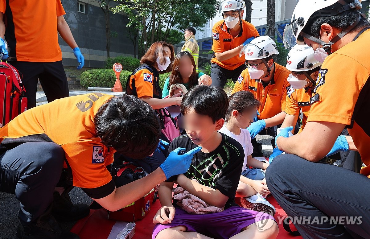 Los bomberos atienden a los niños que escaparon de un complejo de apartamentos en Incheon, al oeste de Seúl, el 1 de agosto de 2024, cuando un estacionamiento quedó envuelto en llamas después de que un vehículo eléctrico explotara espontáneamente. (Yonhap) 